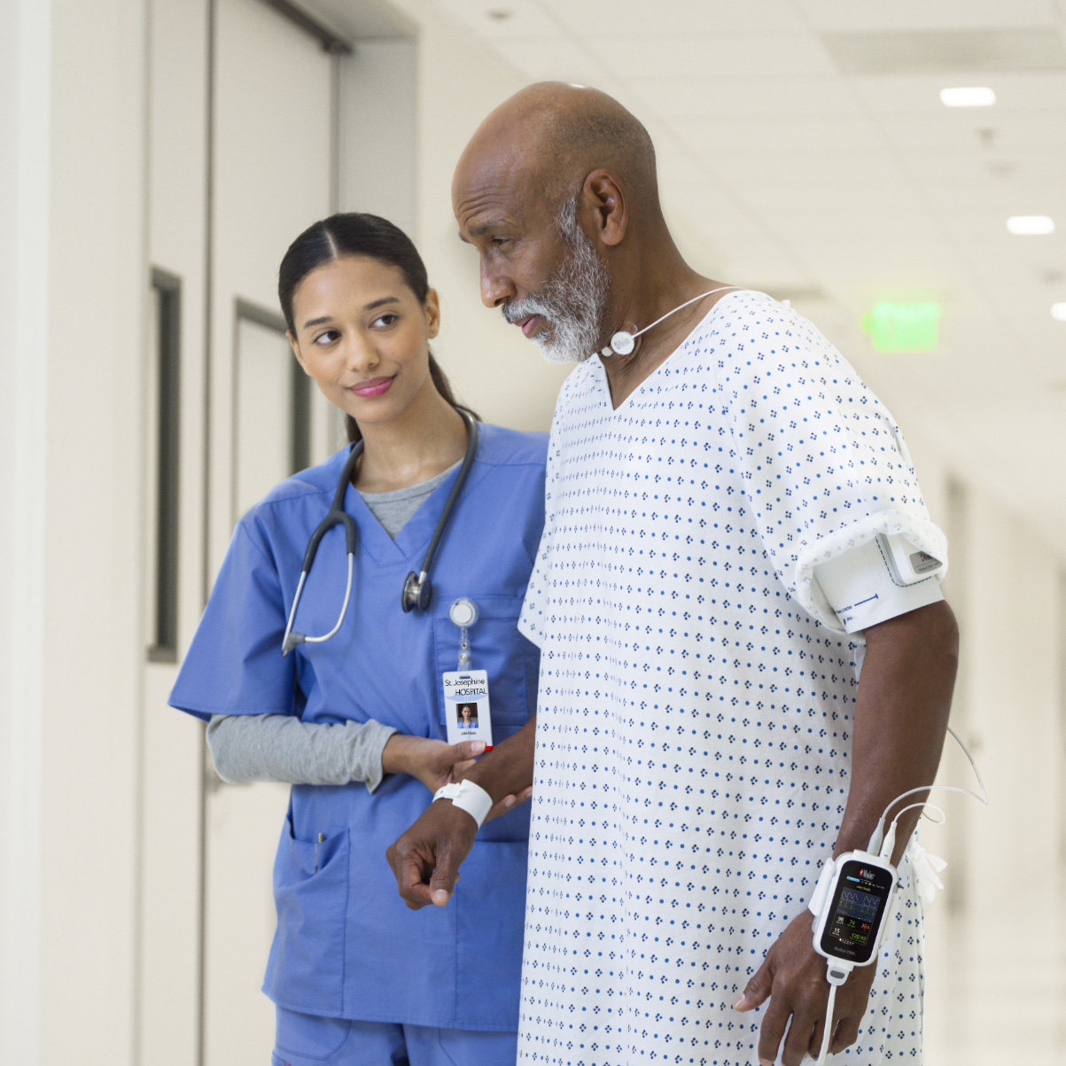 Patient à la peau foncée aidé par une infirmière en blouse d'hôpital et portant un moniteur Masimo Radius VSM. 